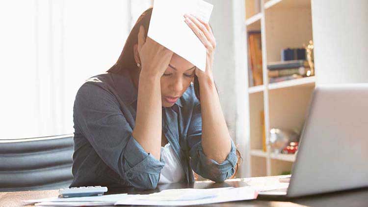 Mujer se agarra la cabeza frente a computadora portátil.