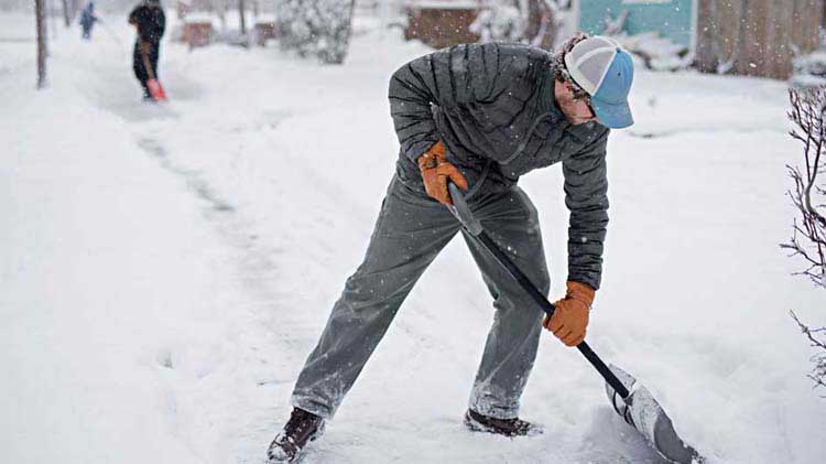 Dueño de empresa paleando nieve para limpiar una acera para prevenir resbalones y caídas en el lugar de trabajo.