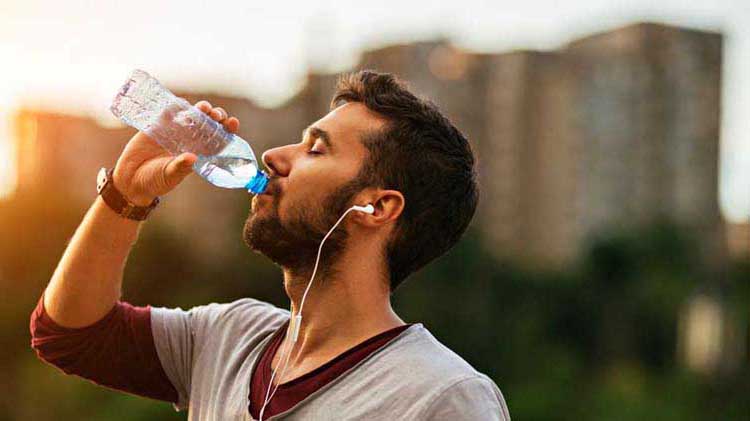 Hombre atlético bebiendo agua en un día húmedo para evitar enfermedades relacionadas con el calor.