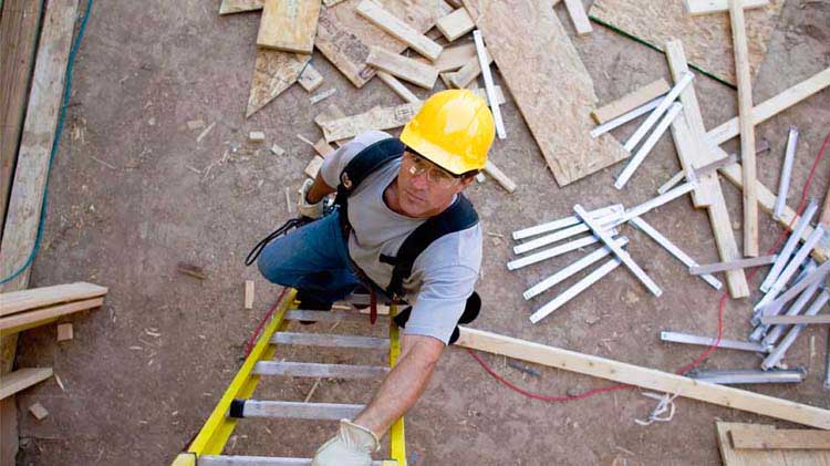 Hombre con casco mira hacia arriba mientras sube con seguridad una escalera.