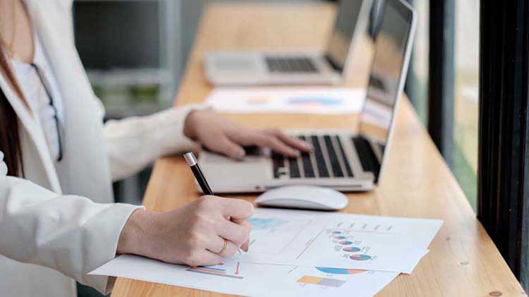 Una mujer con unos papeles revisa su prospecto en la computadora.