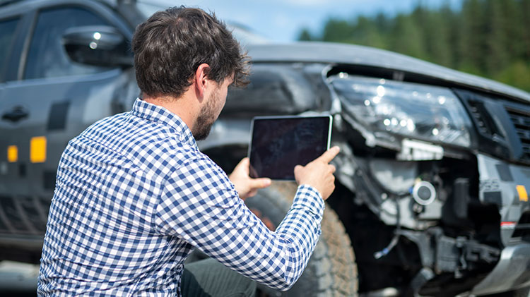Un hombre toma una foto de su carro dañado para documentar un reclamo de seguro de carros.