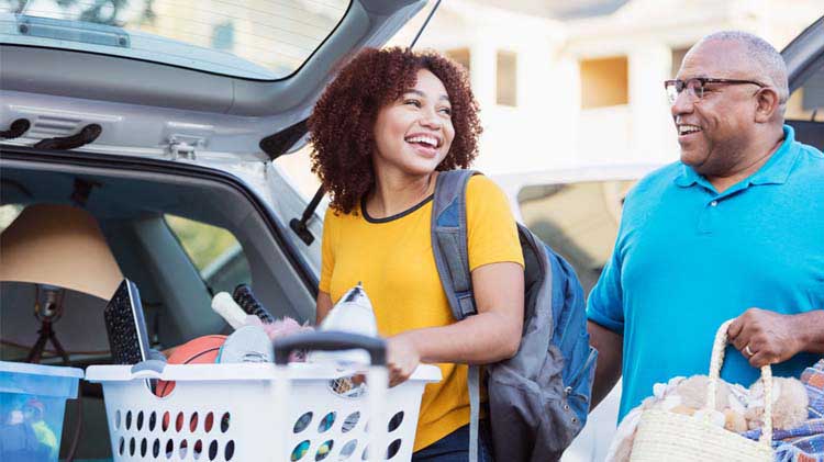 Una mujer joven, junto a su padre, se prepara para ir a la universidad y carga en su carro una canasta de ropa llena de artículos.