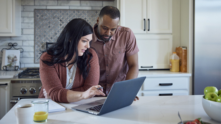 En la cocina, una pareja llena una solicitud de seguro de carros usando su computadora portátil.