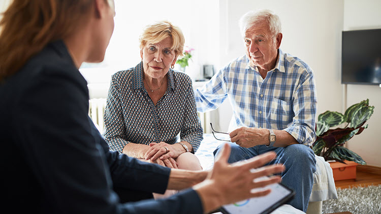 Una mujer y una pareja mayor hablando en una sala.