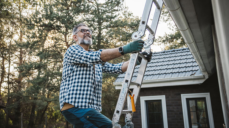 Un hombre sube una escalera para limpiar el techo de escombros propensos a incendiarse.