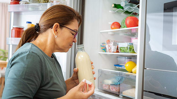 Una mujer huele la leche en el refrigerador para verificar si la comida se ha echado a perder.