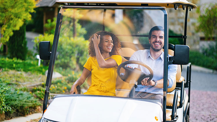 Pareja manejando un carrito de golf por un sendero.