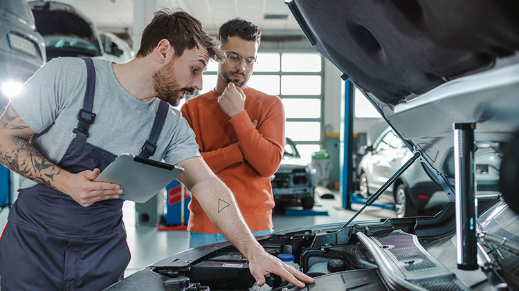 Un mecánico mostrando a un cliente los daños de un carro en un taller de carrocería.