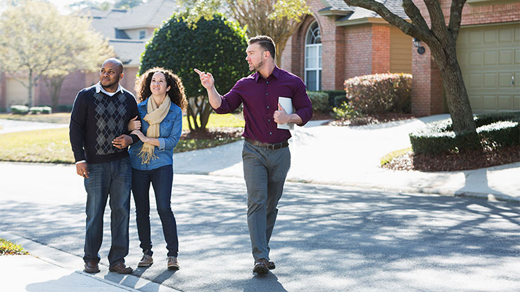 Una pareja explora un vecindario con un corredor de bienes raíces buscando una vivienda.