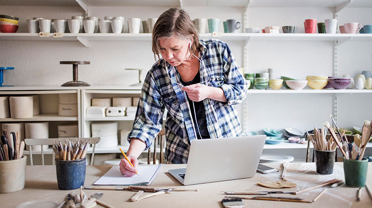Una mujer artista y propietaria de una pequeña empresa hace un inventario en la computadora en su taller de cerámica.