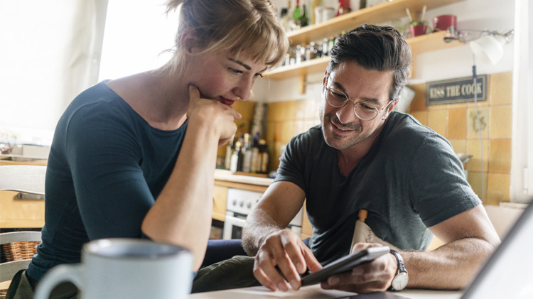 Una pareja sentada en la mesa de la cocina usando un teléfono celular inteligente.
