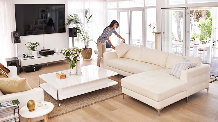 Una mujer arreglando cojines en el sofá mientras prepara una vivienda para la venta.