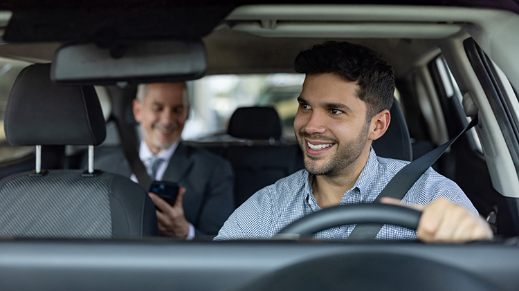 Un sonriente conductor de viajes compartidos mira por el retrovisor a su pasajero.