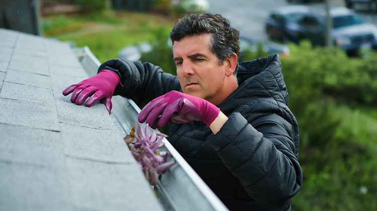 Un hombre con guantes hace mantenimiento al techo, limpiando los canalones.