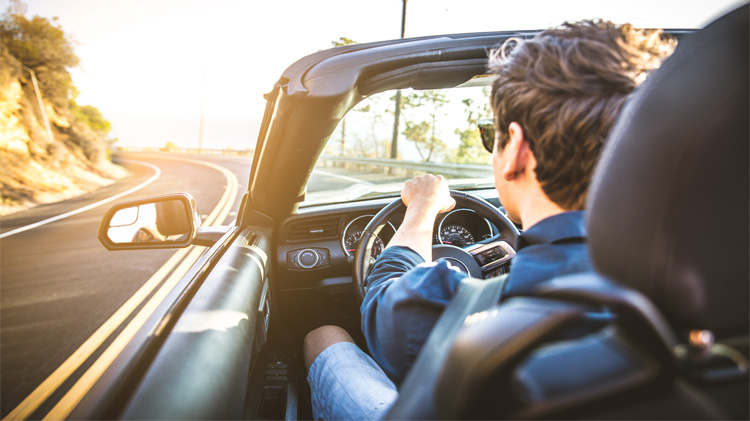 Hombre joven manejando un auto deportivo descapotable en un día de verano.