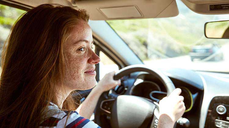 Una adolescente manejando con ambas manos en el volante.