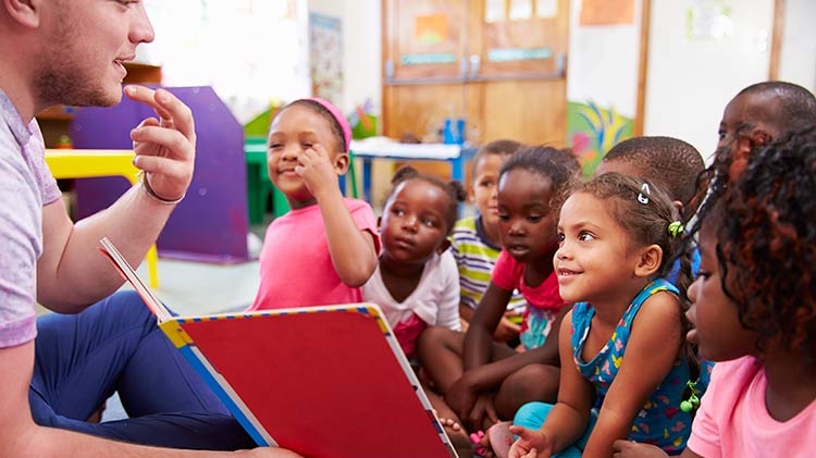Un hombre está haciendo voluntariado en un aula y leyendo a niños.