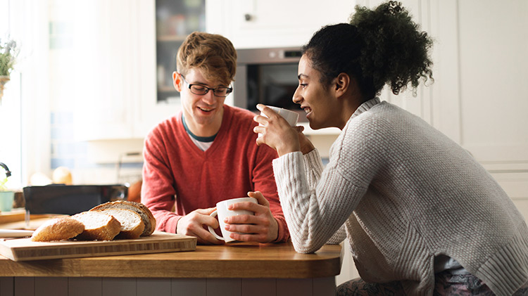 Pareja joven hablando sobre seguros mientras toman café en su cocina.
